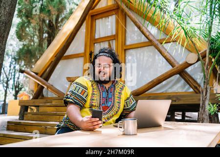 Smiling man with laptop using mobile phone at table Stock Photo