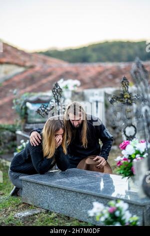 Man consoling woman at tombstone at cemetery Stock Photo