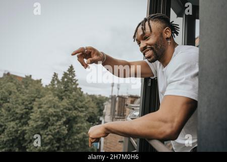 Smiling young man leaning on railing and pointing out Stock Photo