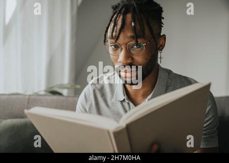 Young man wearing eyeglasses holding book at home Stock Photo