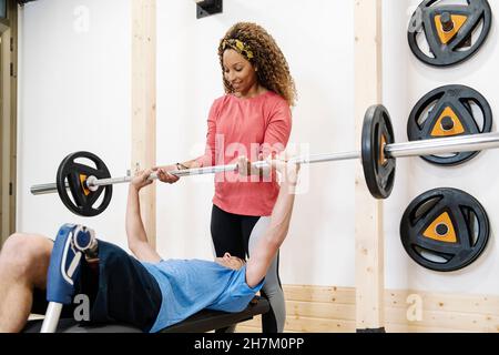 Female instructor helping disabled man weightlifting in gym Stock Photo