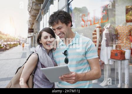 Cheerful couple using digital tablet while standing by clothing store Stock Photo