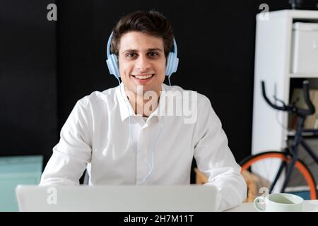 Smiling creative businessman with headphones using laptop in office Stock Photo