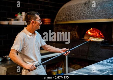 Pizza maker preparing pizza in oven at restaurant Stock Photo