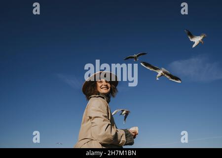 Smiling woman in overcoat feeding seagulls Stock Photo