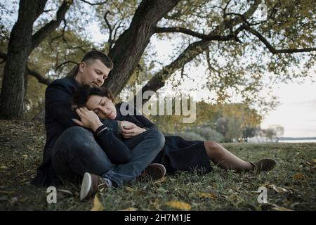Loving couple relaxing on grass in front of tree Stock Photo