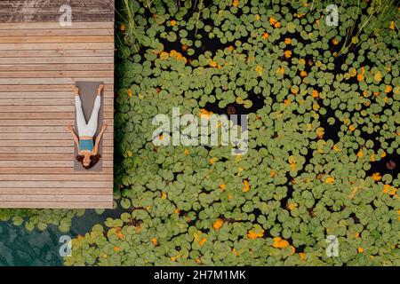 Woman lying on exercise mat while doing yoga at jetty Stock Photo