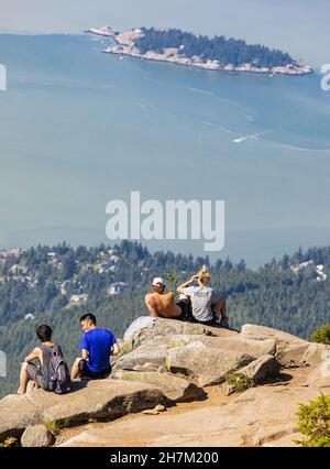 A group of young hikers sitting on a cliff and enjoying the view from the Eagle Bluffs in Cypress Provincial Park, Canada. Concept photo hiking, copy Stock Photo