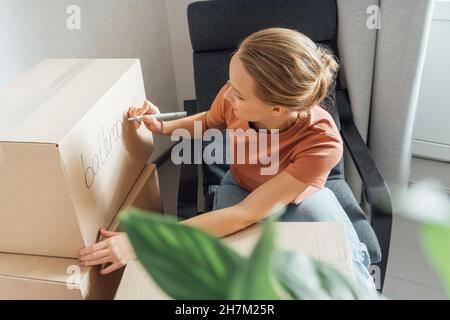 Woman writing on cardboard box in new apartment Stock Photo