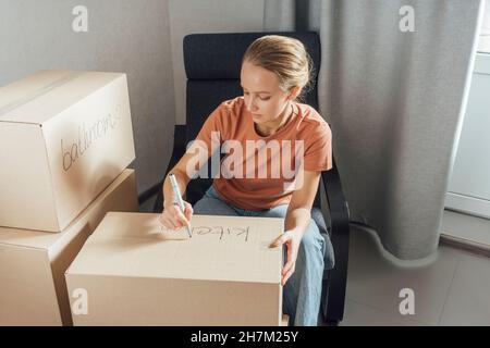 Woman writing with felt tip pen on cardboard box at home Stock Photo