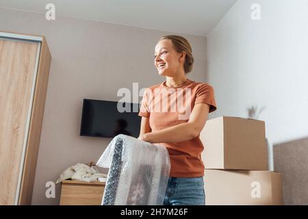 Smiling woman removing bubble wrap from picture frame at home Stock Photo