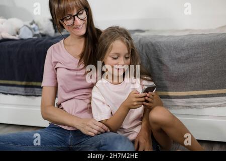 Daughter using smart phone with mother at home Stock Photo