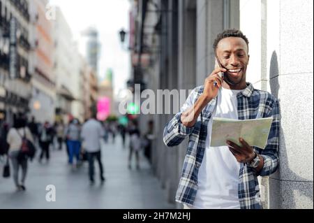 Young man checking map and talking on mobile phone at city street Stock Photo