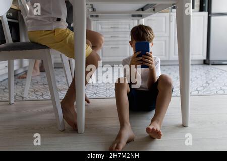 Boy using mobile phone under table at home Stock Photo