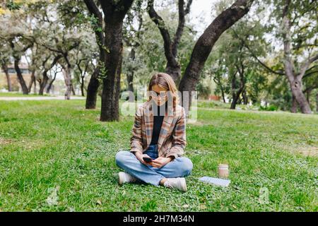 Smiling businesswoman text messaging through smart phone on grass in park Stock Photo