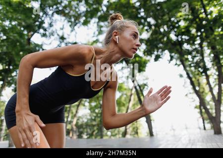 Determined woman with in-ear headphones running at park Stock Photo