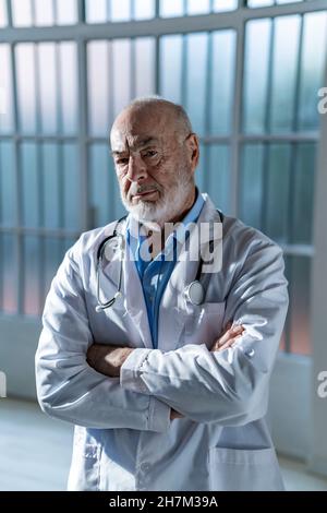Happy senior doctor in lab coat standing with arms crossed Stock Photo