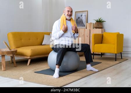 Smiling senior man holding water bottle on fitness ball at home Stock Photo