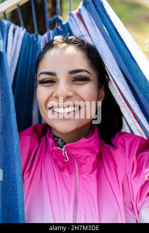 Woman's hand holding smart phone on video call relaxing in hammock at park Stock Photo