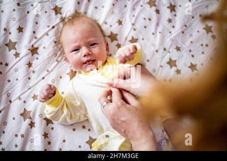 Top view portrait cute newborn redhead baby in childish overalls lying crib during mother dressing Stock Photo