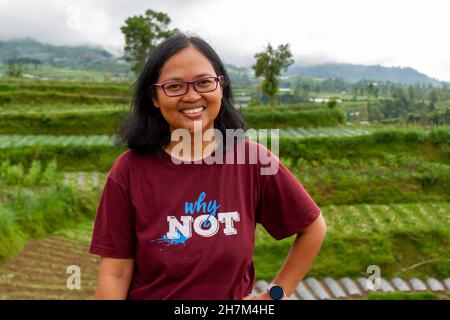 An asian woman smiling in the countryside with a background of vegetables planted on a terrace of a mountain, nature concept Stock Photo
