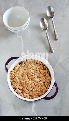 Fresh baked apple crumble in small casserole dish on light marble background in vertical orientation. Stock Photo