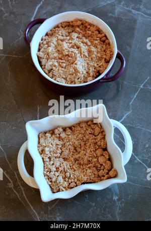 Fresh baked apple crumbles in small casserole dishes on dark marble background in vertical orientation. Stock Photo
