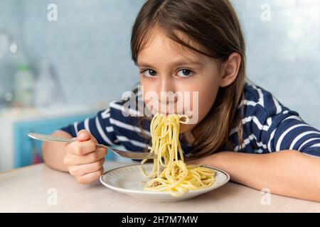 Kids eat pasta. Healthy lunch for children. Toddler kid eating spaghetti Bolognese in a blue kitchen at home. Preschooler child try noodles for dinner Stock Photo