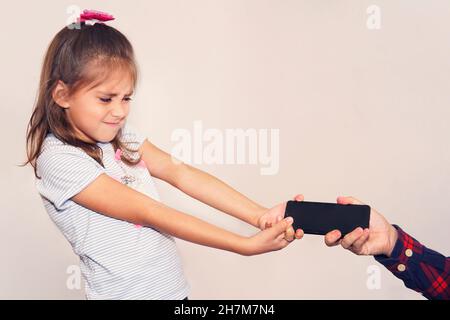 The father takes the phone from his daughter. Children's addiction to mobile games. A thief stole a child's phone. Angry dissatisfied girl snatches th Stock Photo