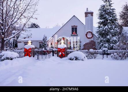 A festive, welcoming home, nicely decorated with ribbons a wreath and glowing candles, blanketed with snow and ready for Holiday celebrations. Stock Photo