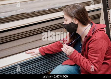 Woman in mask is located in store. She chooses paneling for the walls. Close up Stock Photo