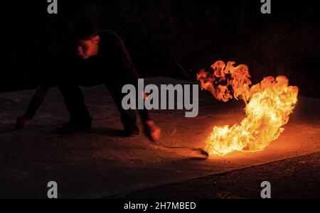 Fascinating and dangerous. Man manipulate with burning poi in dark. Burning fuel and energy. Sparks and lights. Night show. Fire performance. Flirt wi Stock Photo