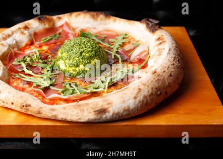 Pizza with Parma ham, arugula, and burrata cheese with green pesto. A tasty dish.Culinary photography. Suggestion to serve the dish. Stock Photo