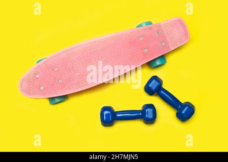Skateboard and dumbbells on yellow background Stock Photo