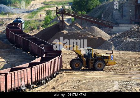 Large heavy front-end loader loading sand it to the freight train. Heavy mining work in a quarry Stock Photo