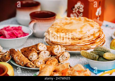 Dishes of the traditional Belarusian cuisine - pancakes, pancake rolls and pickled cucumbers. Attribute of traditional folk celebration of Maslenitsa Stock Photo