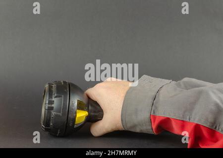 A man in workwear is holding a hand flashlight. Safety first is a concept. Selective focus. Stock Photo