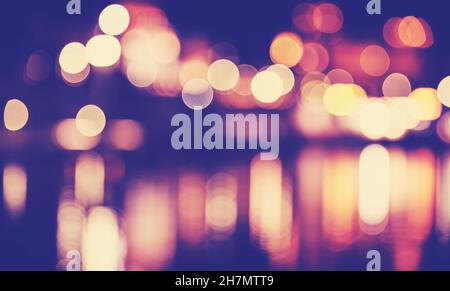 Blurred city lights reflected in water at night, color toned urban abstract background. Stock Photo