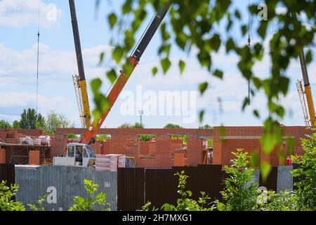 View of a construction site with a crane and a house under construction through trees and green leaves. Selective focus Stock Photo
