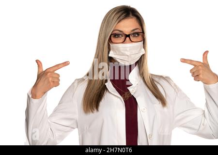 Young beautifuls female doctor with eyeglasses pointing on her  face medical mask on a white background Stock Photo
