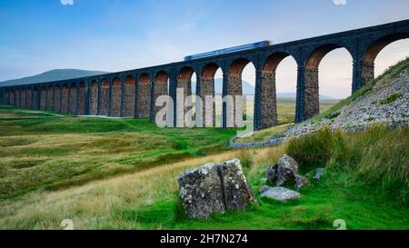 Scenic countryside valley (locomotive, iconic Ribblehead Viaduct landmark, sunlight on brick arches, high hills) - North Yorkshire Dales, England UK. Stock Photo