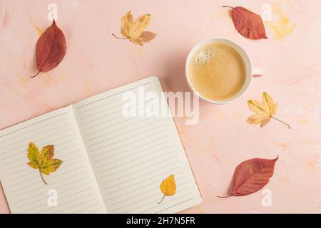 Mock up. Open lined notepad on desk workspace, coffee and yellow autumn leaves, pink background. Creative concept, empty page, note paper for school. Top view, copy space Stock Photo