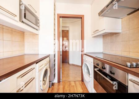 Kitchen with wood-colored countertop, open dishwasher, ceramic hob, oven and washing machine with dark wooden floor in vacation rental apartment