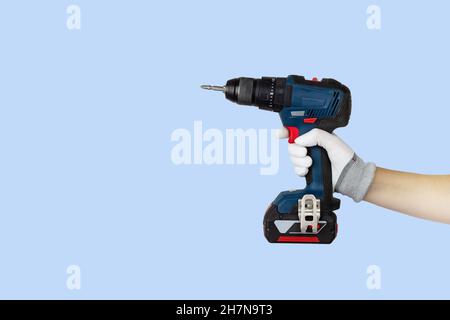 Gloved hands holding screwdriver, drill construction tools. Work tools on blue background Stock Photo