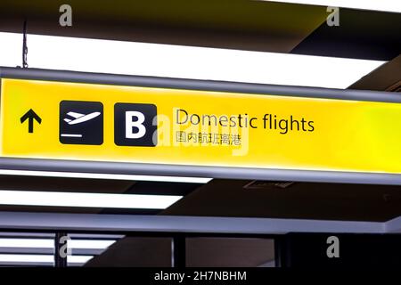 Bright illuminated yellow and black airport signs with arrows and plane icons and the title in Chinese: 'Domestic flights'. Stock Photo