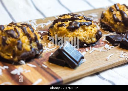 Close up of Coconut Macaroons with Dark Chocolate Drizzle Served on Wooden Serving Board Garnished with Chocolate Pieces and Coconut Shavings. Selecti Stock Photo