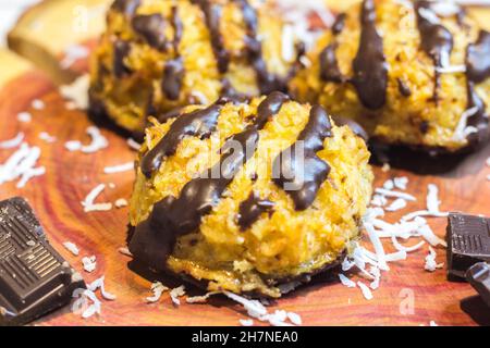 Coconut Macaroons with Dark Chocolate Drizzle Served on Cherry Wooden Board Garnished with Chocolate Pieces and Coconut Shavings, Selective Focus Stock Photo