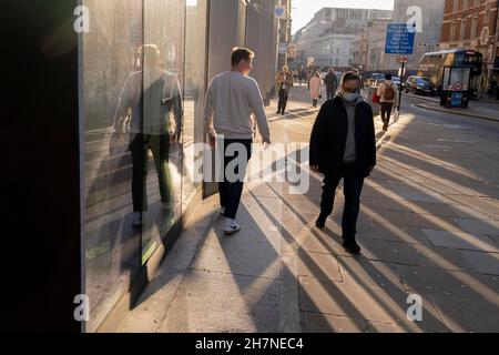 Pedestrians walk through reflected autumn sunlight on Moorgate in the City of London, the capital's financial district, on 23rd November 2021, in London, England. Stock Photo