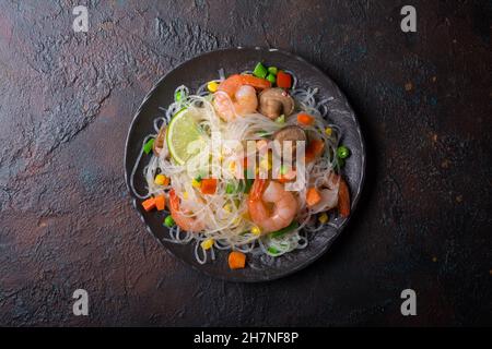 Top view of plate with japanese bean or glass noodles, tasty shrimps, shiitake mushrooms and vegetables on brown concrete background Stock Photo