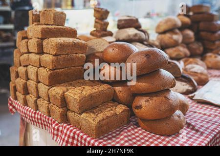 Pile of freshly baked loaves of bread on table at the local market. Many traditional fresh round and square bread loaves for sale. No people. Selective focus. Stock Photo